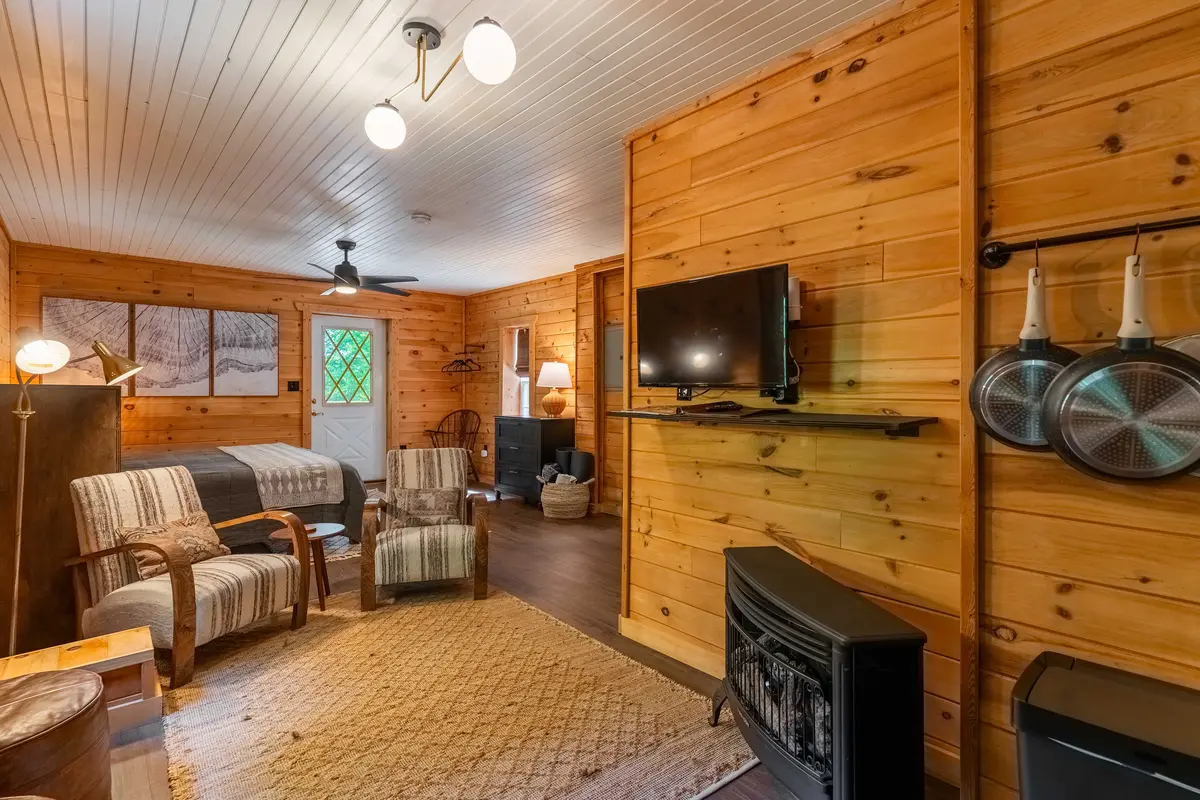 Wide interior view from the kitchen looking toward the bed, seating area, TV, and fireplace inside The Snug cabin in Lake Lure, North Carolina