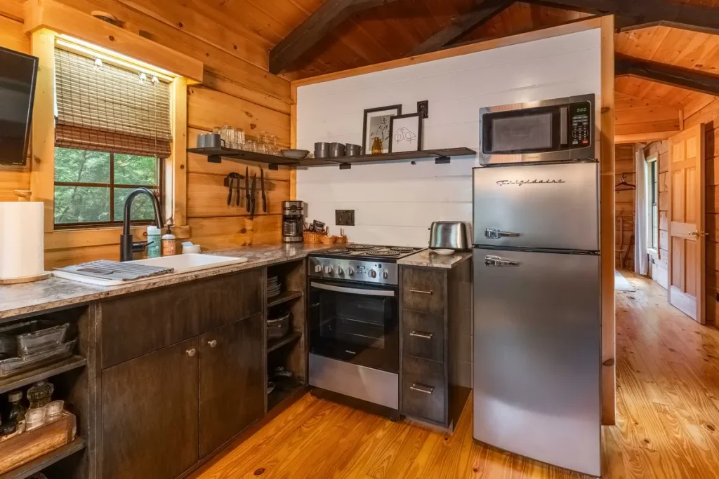 Full kitchen with stove, refrigerator, sink, and open shelving inside The Roost cabin in Lake Lure, North Carolina